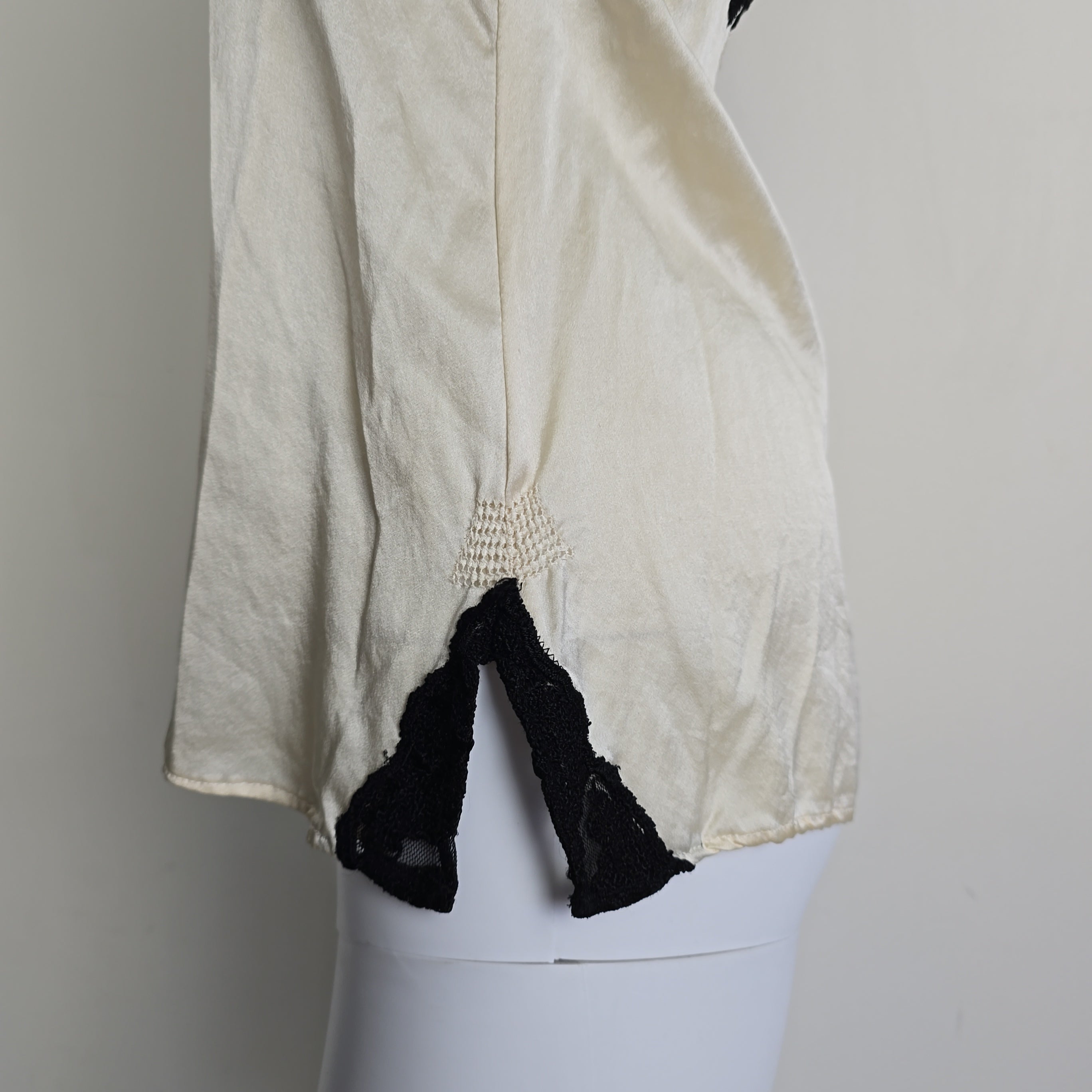 Mannequin wearing a white top with black lace details on a plain background