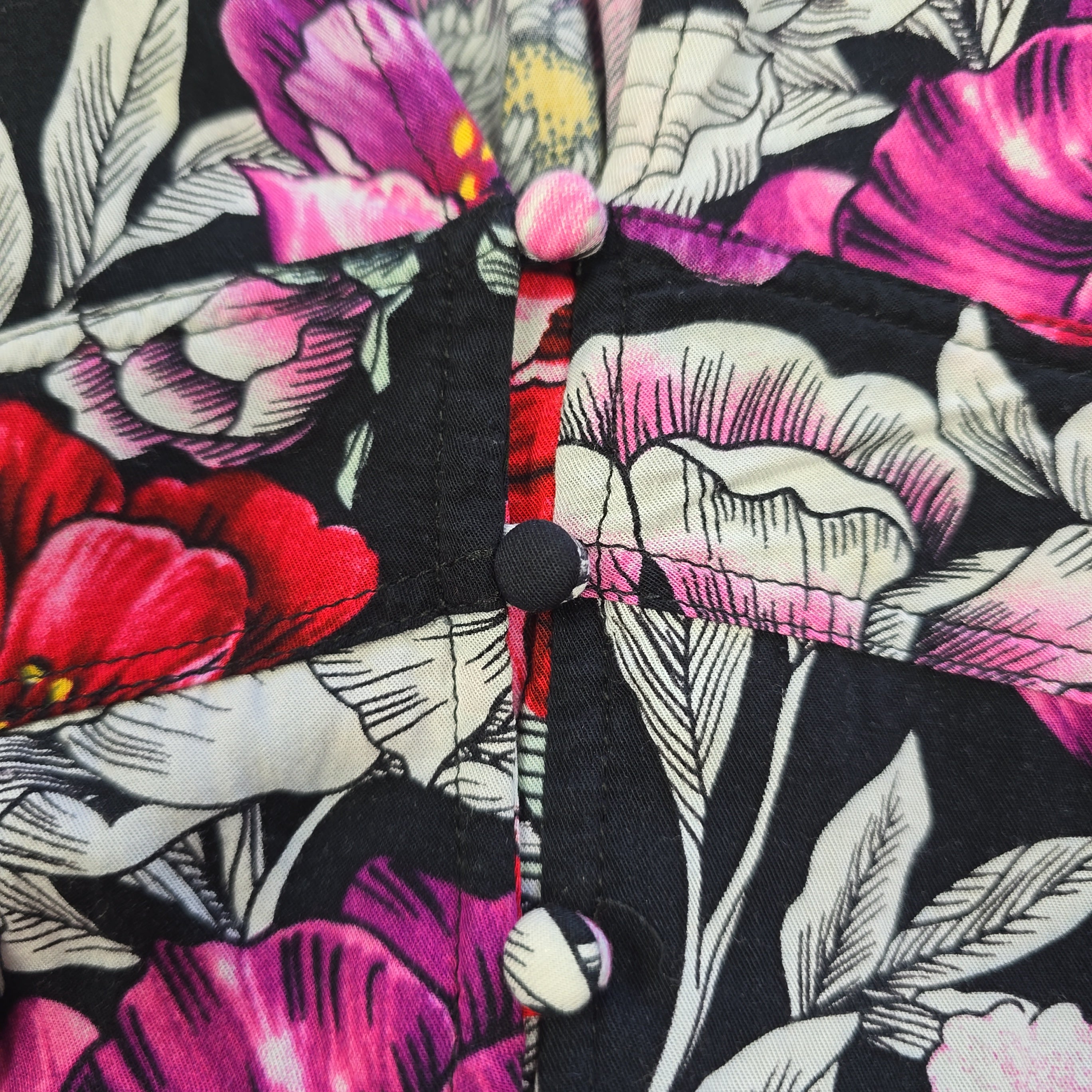 Close-up of a floral patterned shirt with pink, red, and white flowers on a black background.