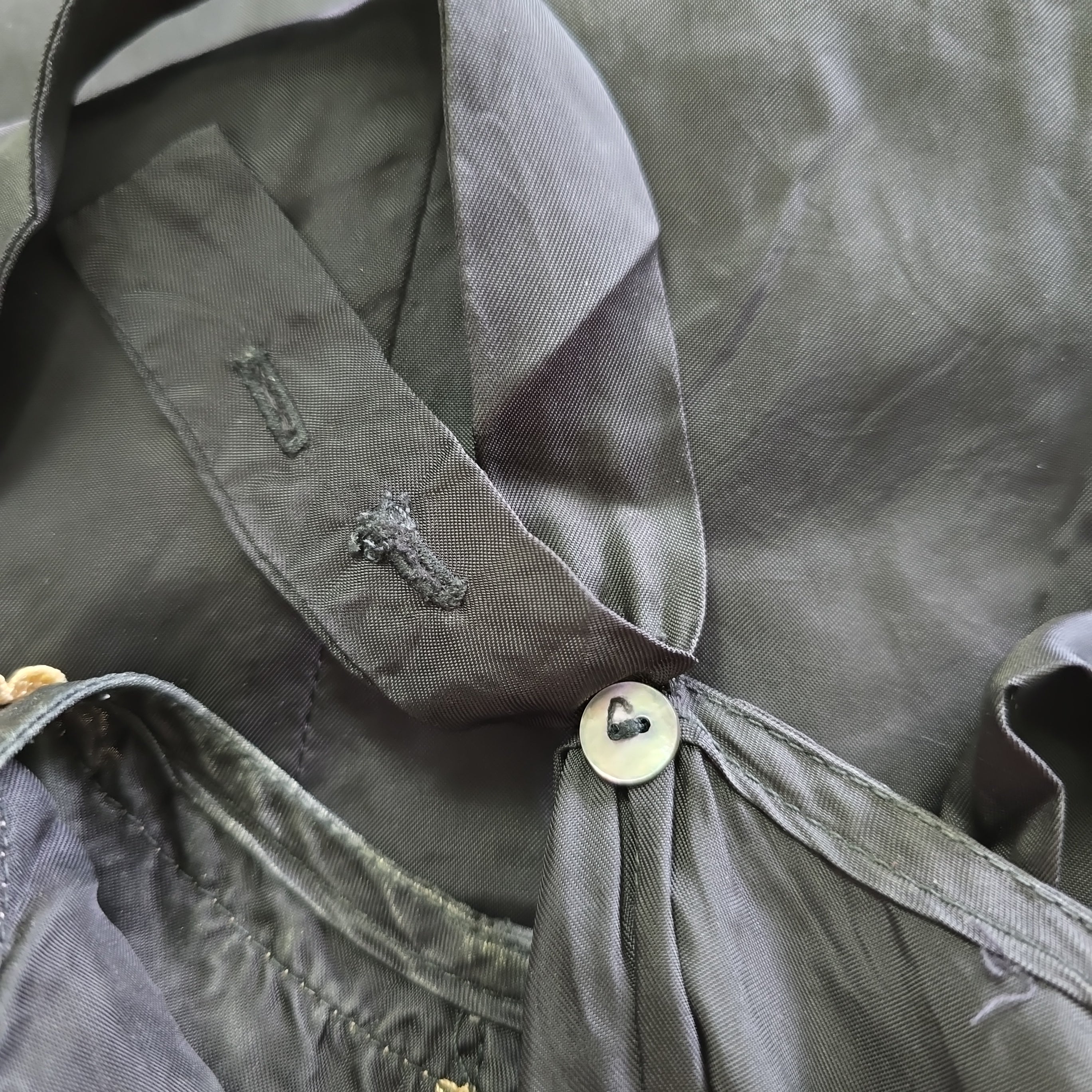 Close-up of a black dress with a button and brand logo