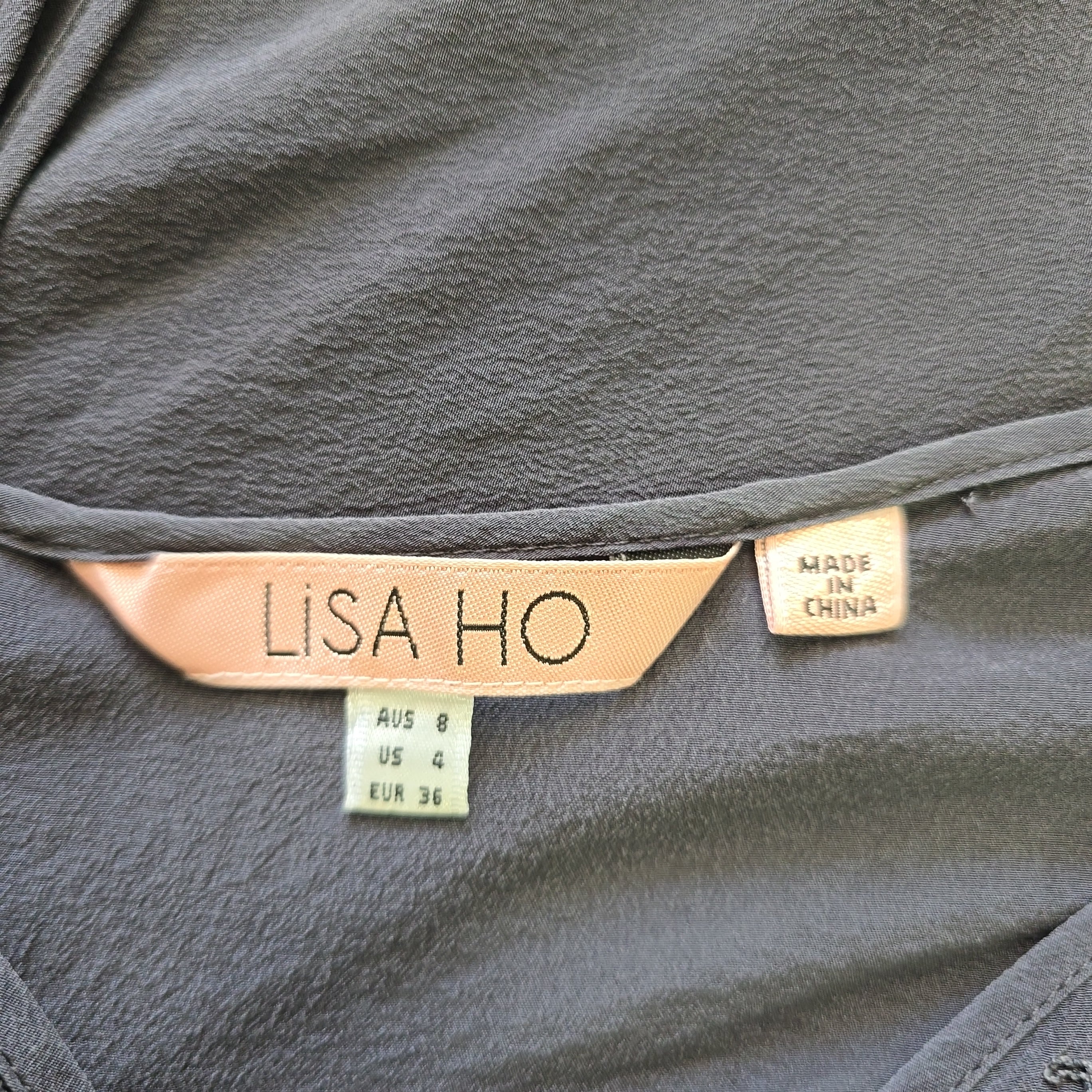 Close-up of a gray garment with a 'Lisa Ho' label on a dark background
