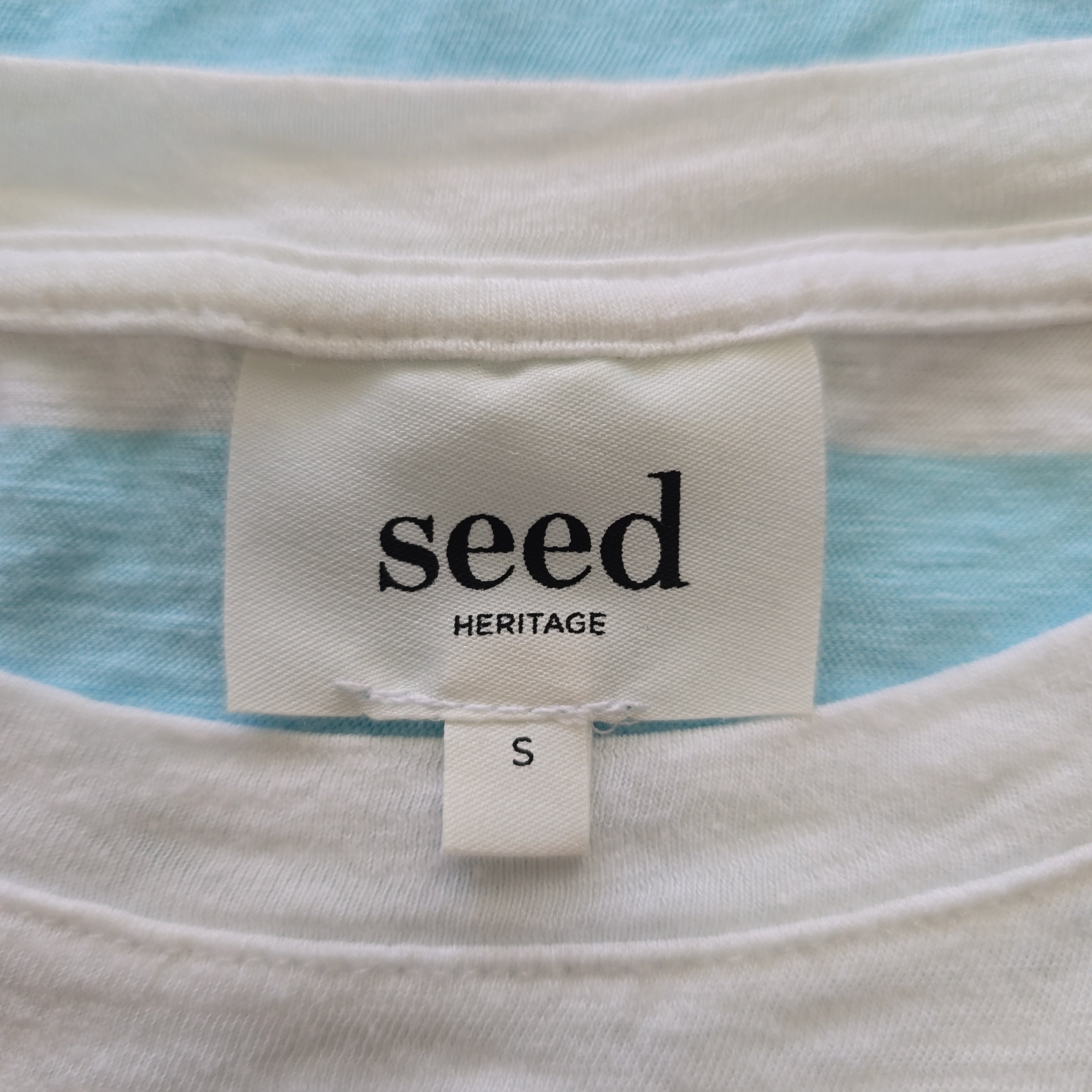 Close-up of a 'seed Heritage' label on a garment with a blue and white striped background.