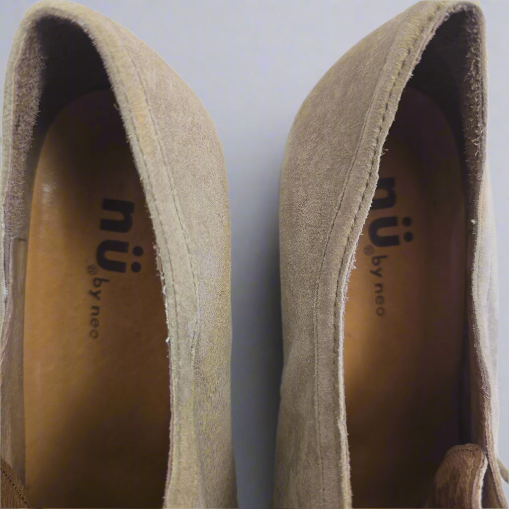 Close-up of brown suede shoes with 'nu by neo' branding on a white background