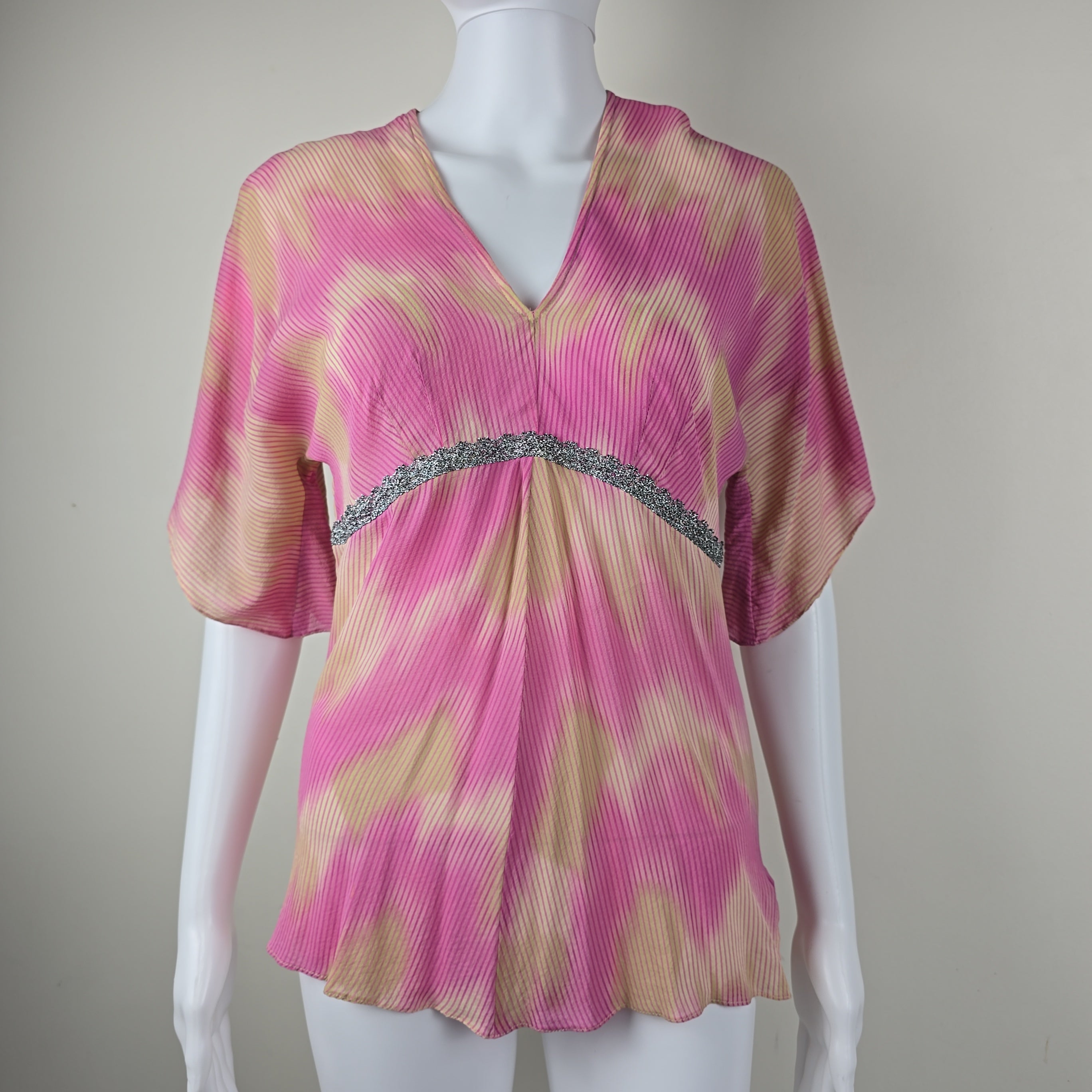 Mannequin wearing a pink and beige top with silver lace on a plain background