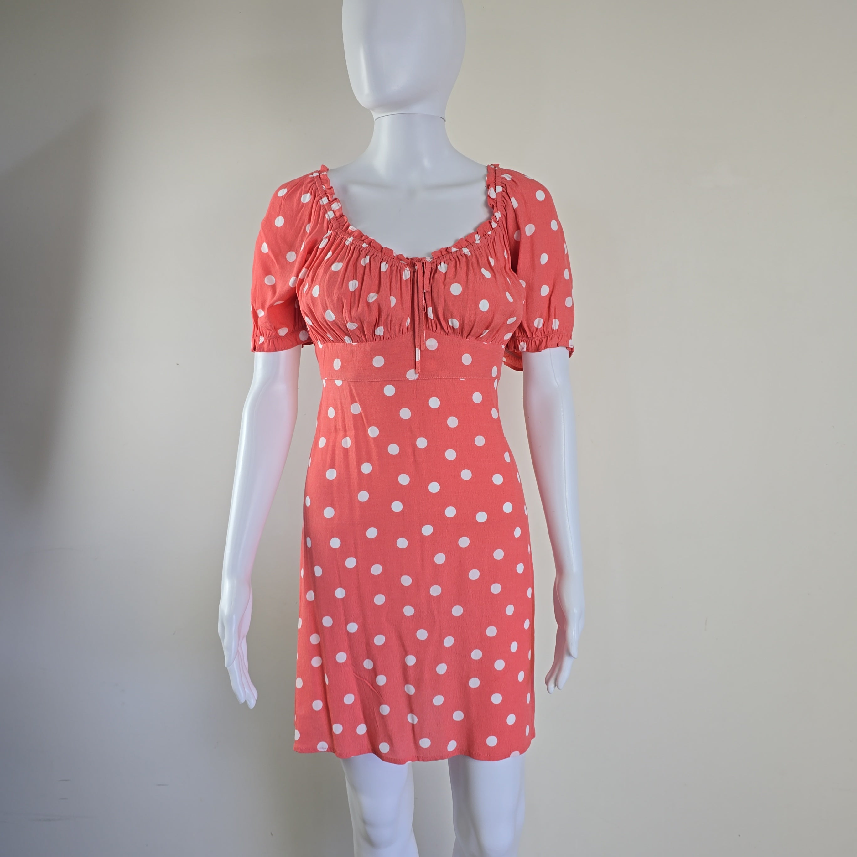 Mannequin wearing a coral dress with white polka dots on a plain background