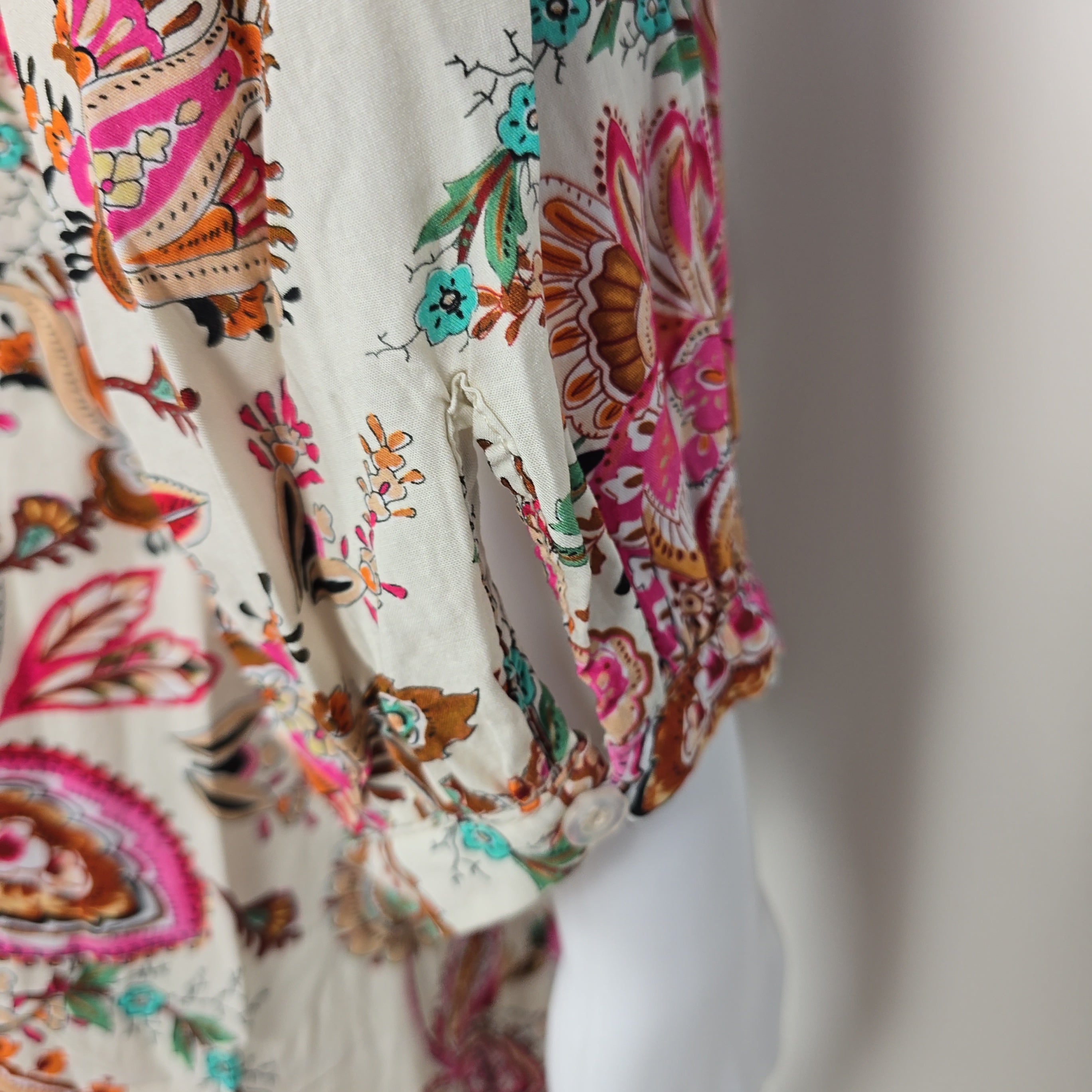 Close-up of a fabric with intricate floral and paisley patterns in brown, pink, and green on a beige background.