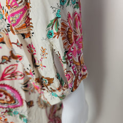 Close-up of a fabric with intricate floral and paisley patterns in brown, pink, and green on a beige background.