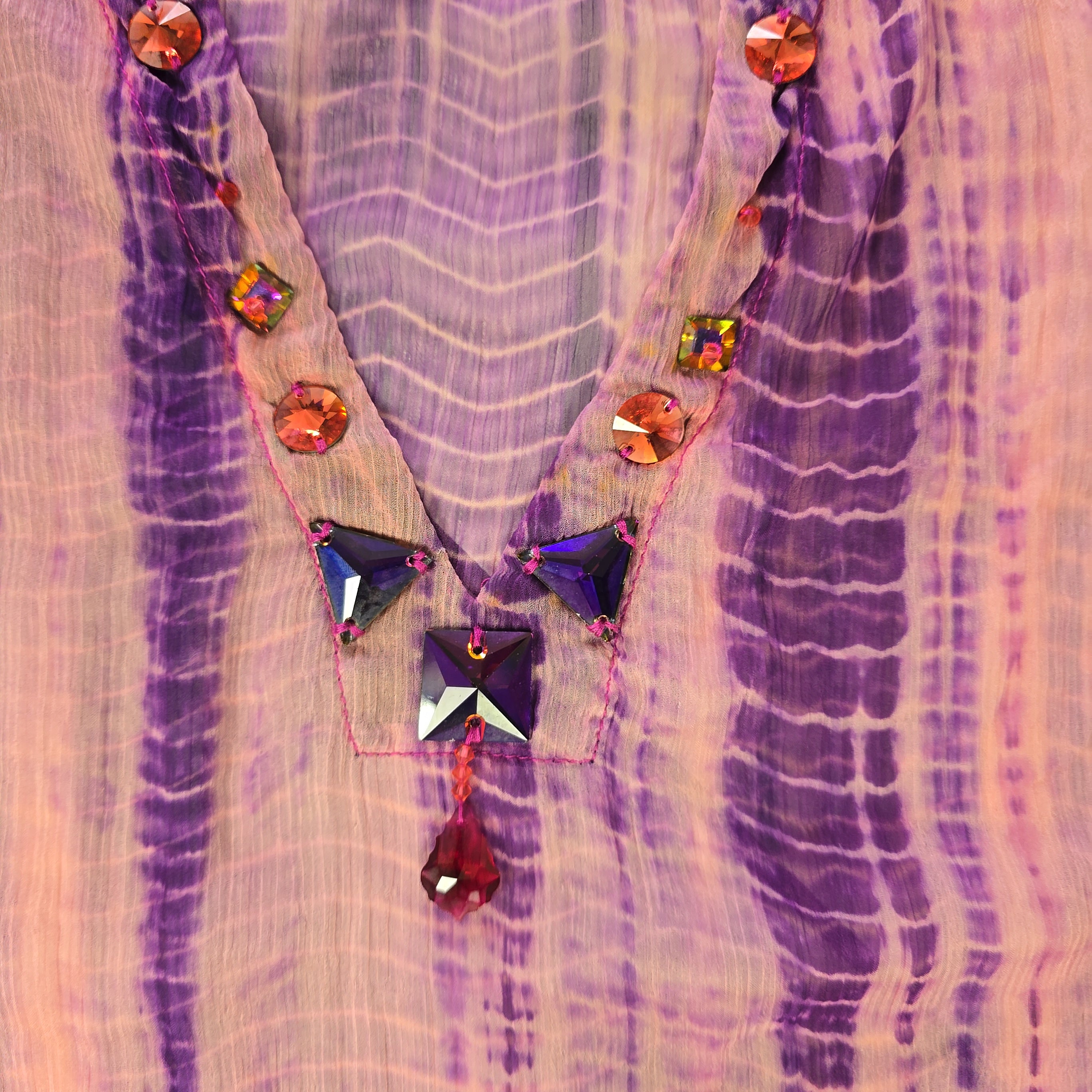 Decorative fabric with purple and pink patterns and colorful gemstones.
