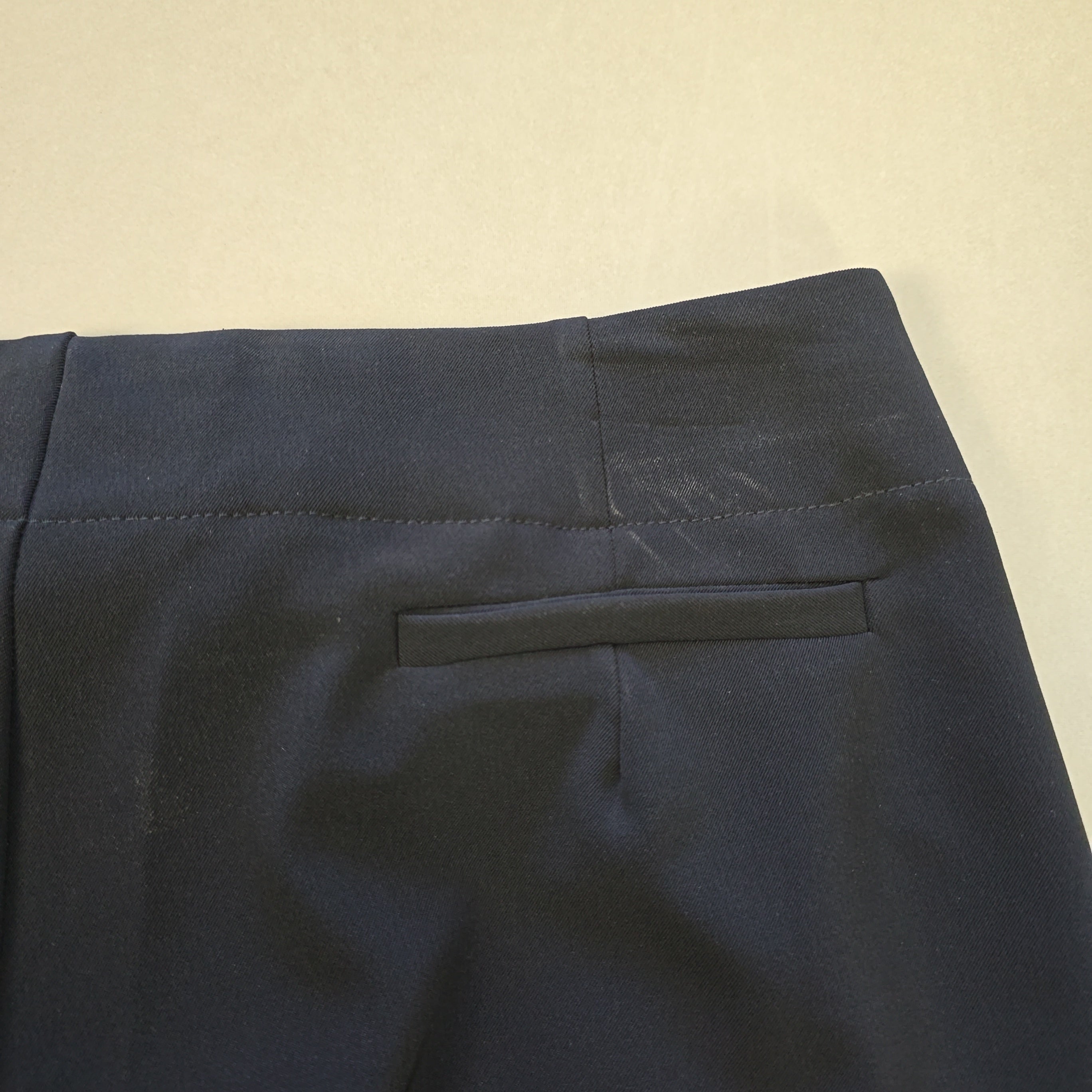 Close-up of dark black pants with a pocket on a beige background