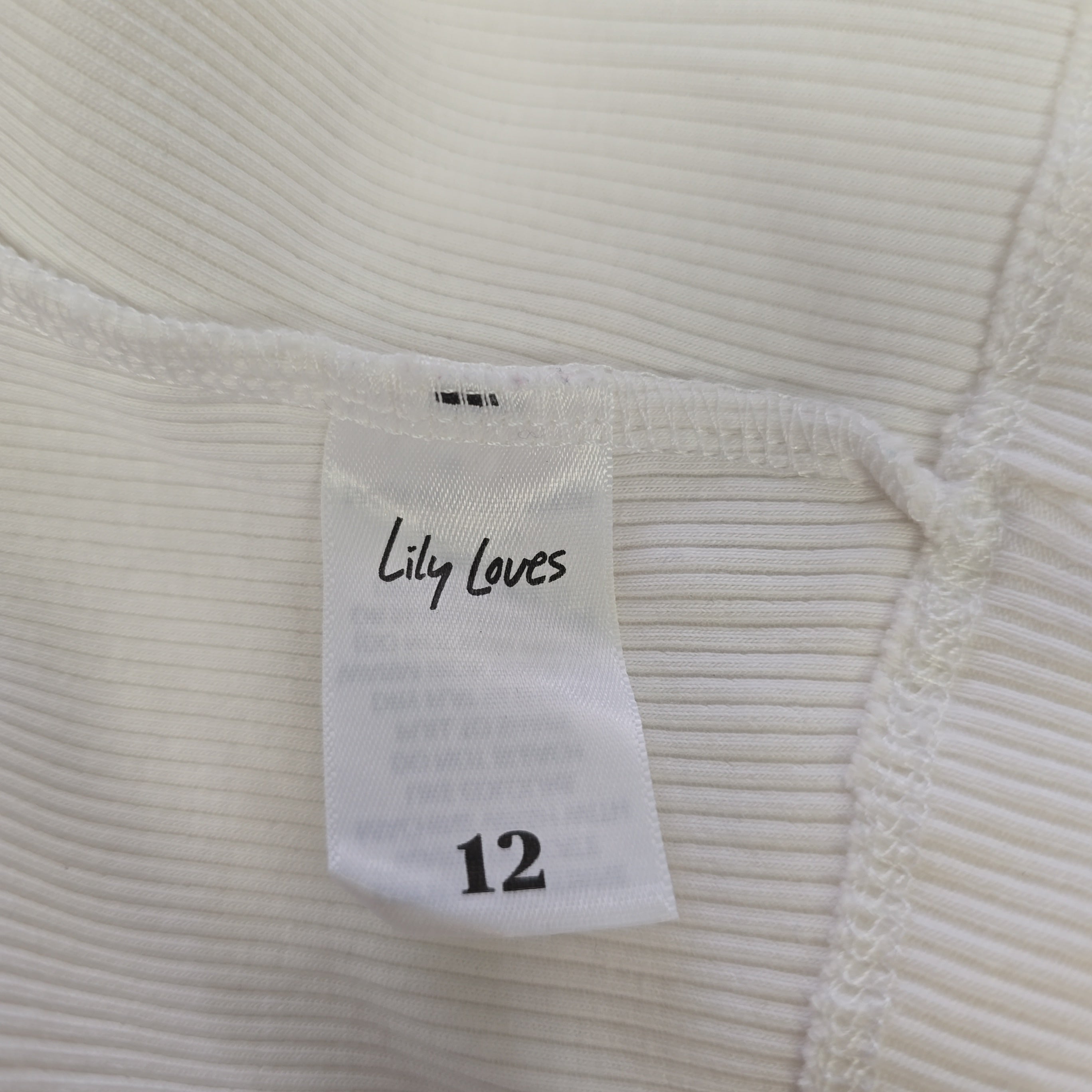 Close-up of a white ribbed fabric with a 'Lily Loves' label on a light gray background