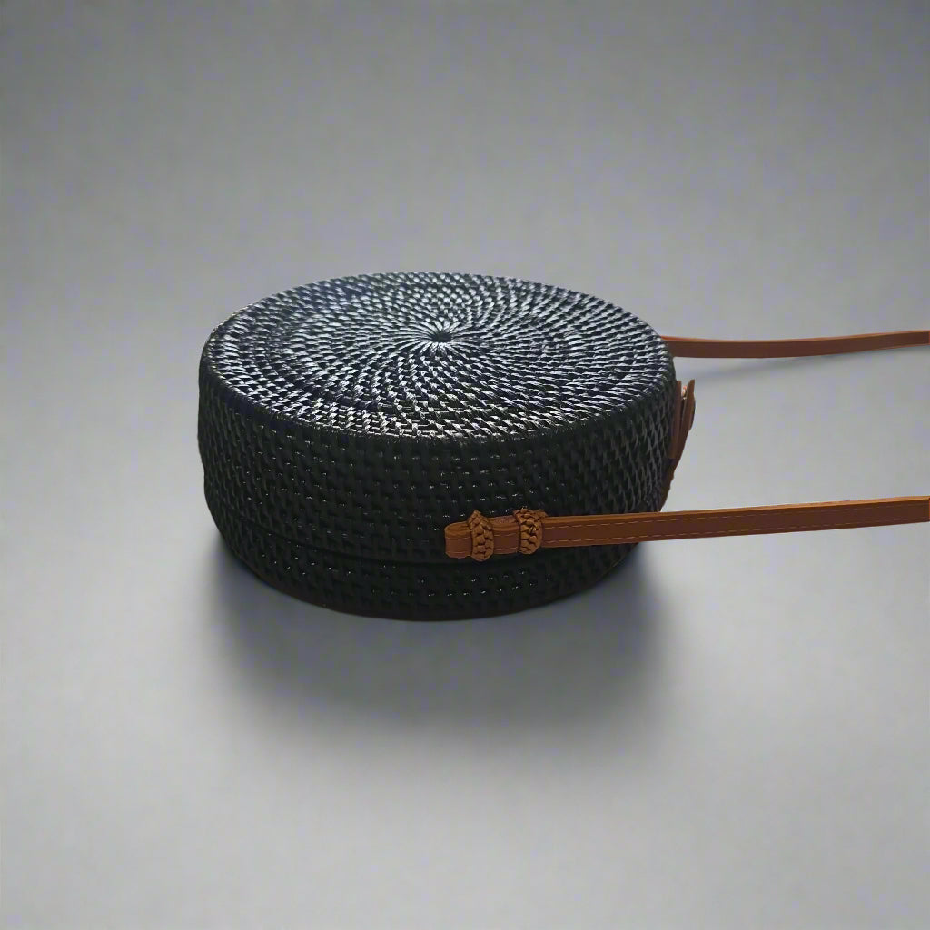 Black woven handbag with a brown strap on a tiled floor