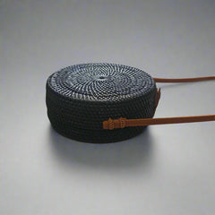 Black woven handbag with a brown strap on a tiled floor