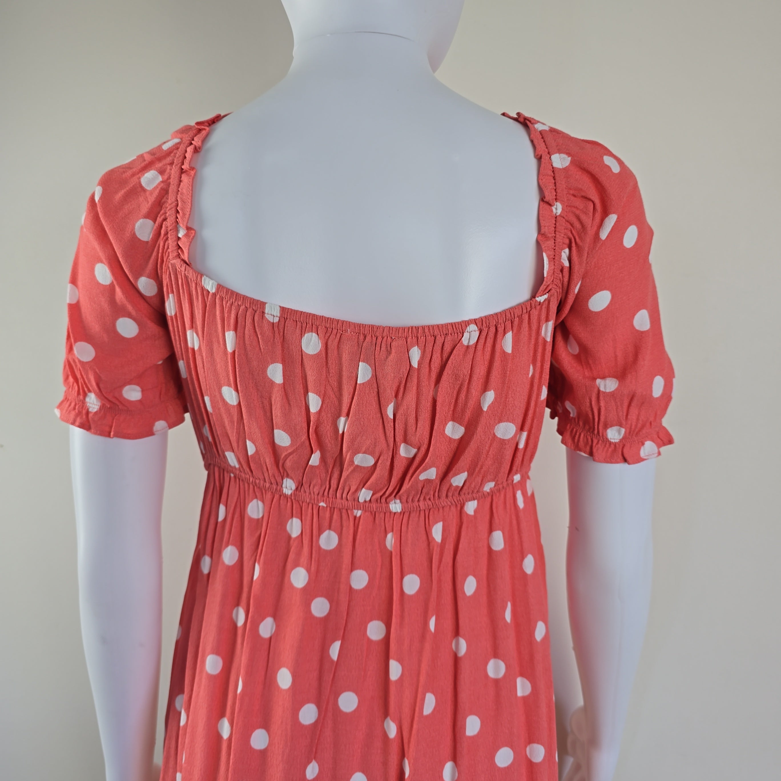 Red dress with white polka dots on a mannequin against a plain background
