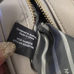 Close-up of a beige handbag with a gold zipper and visible brand label.