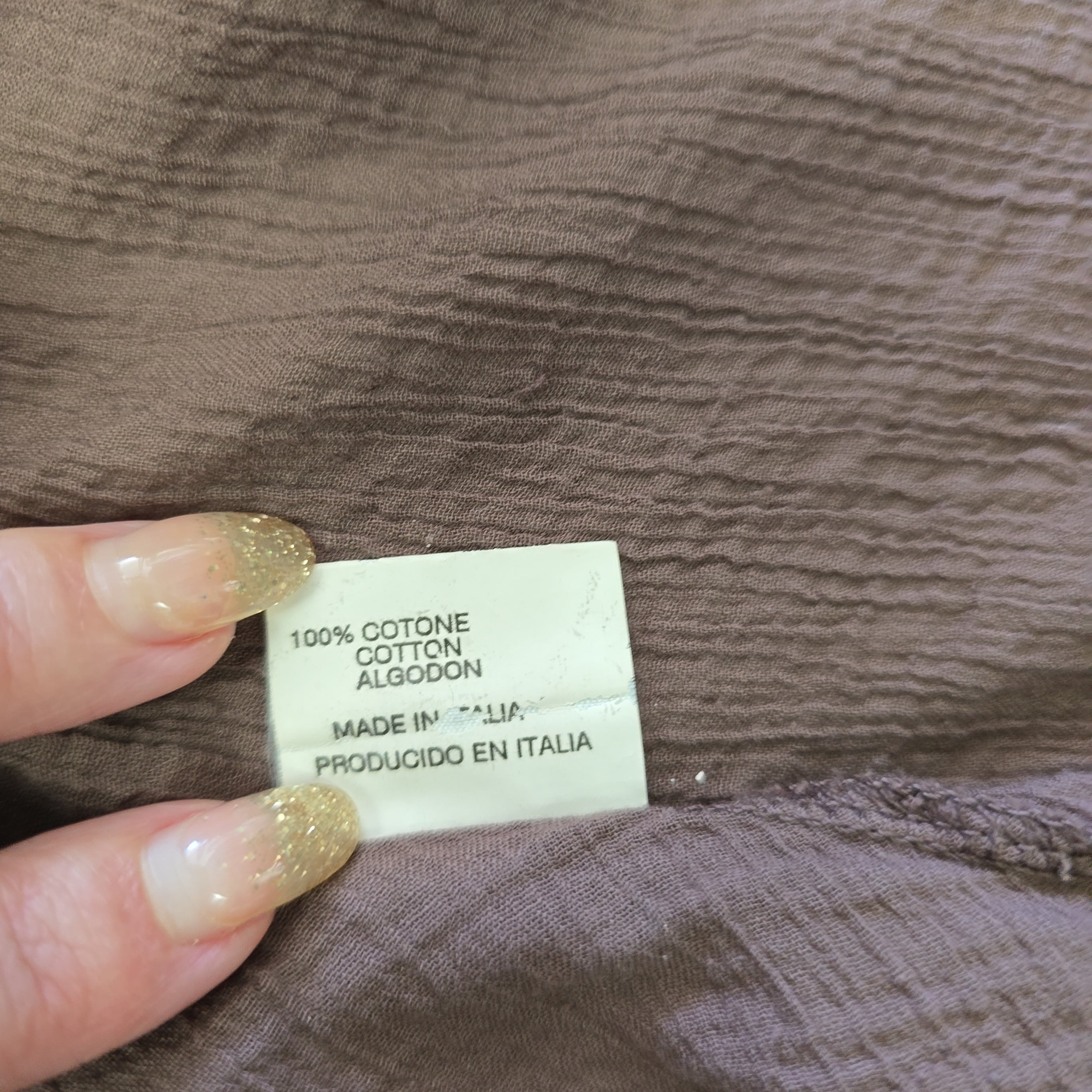 Close-up of a fabric tag on brown material with a hand holding it.