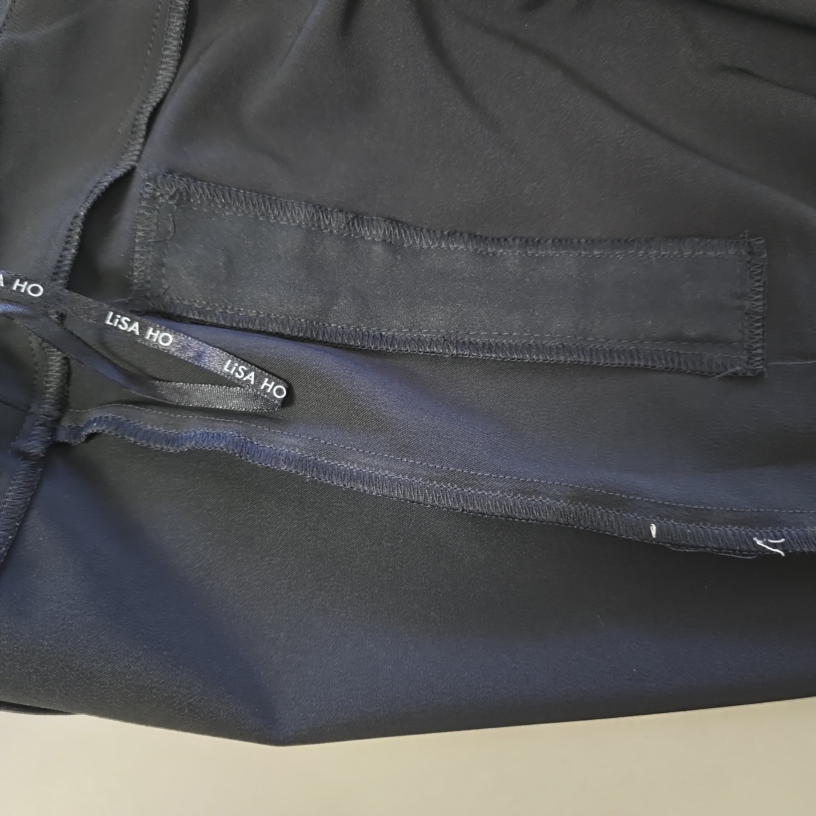 Close-up of a black pants with a visible brand label on a beige background