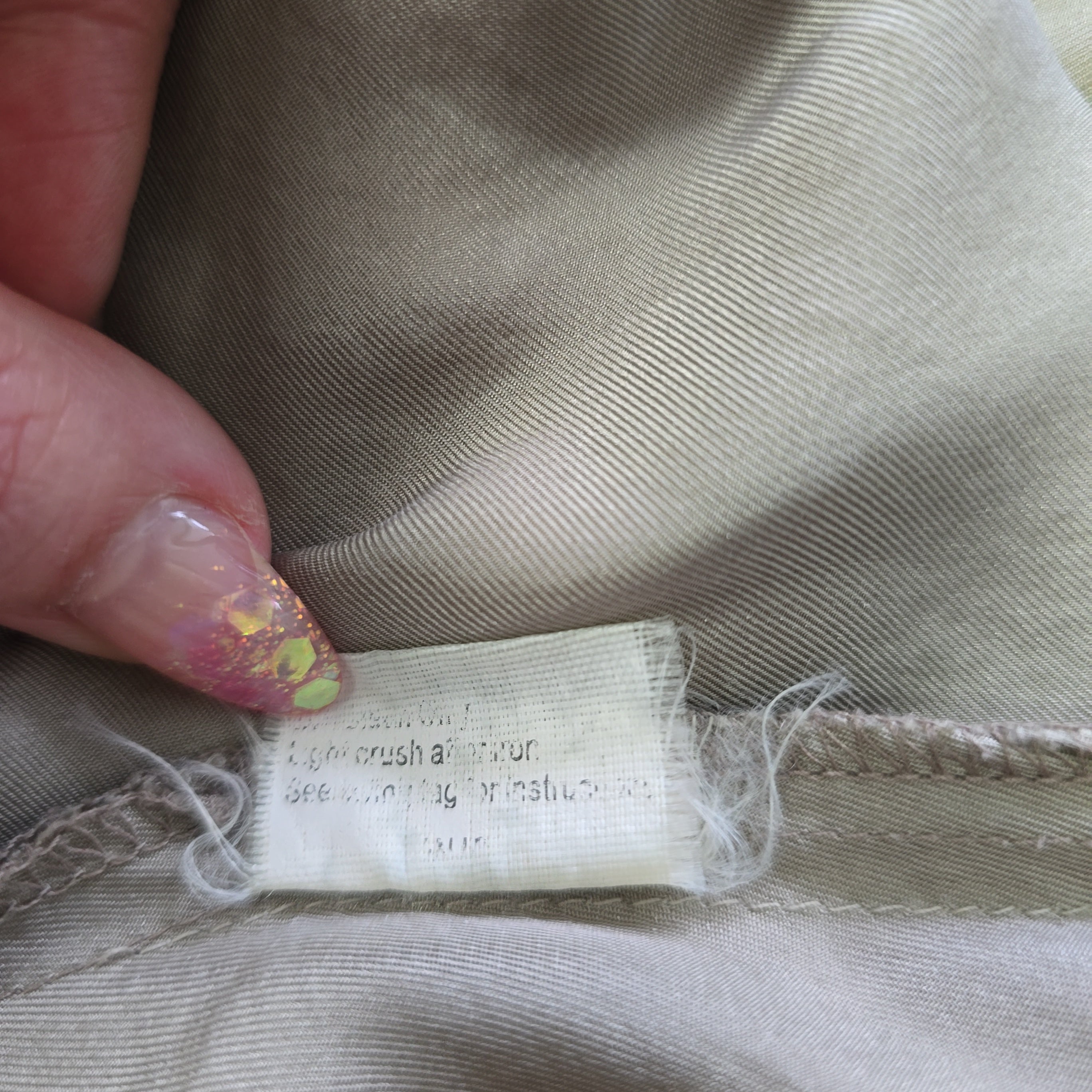 Close-up of a fabric tag on beige fabric with a hand holding it.
