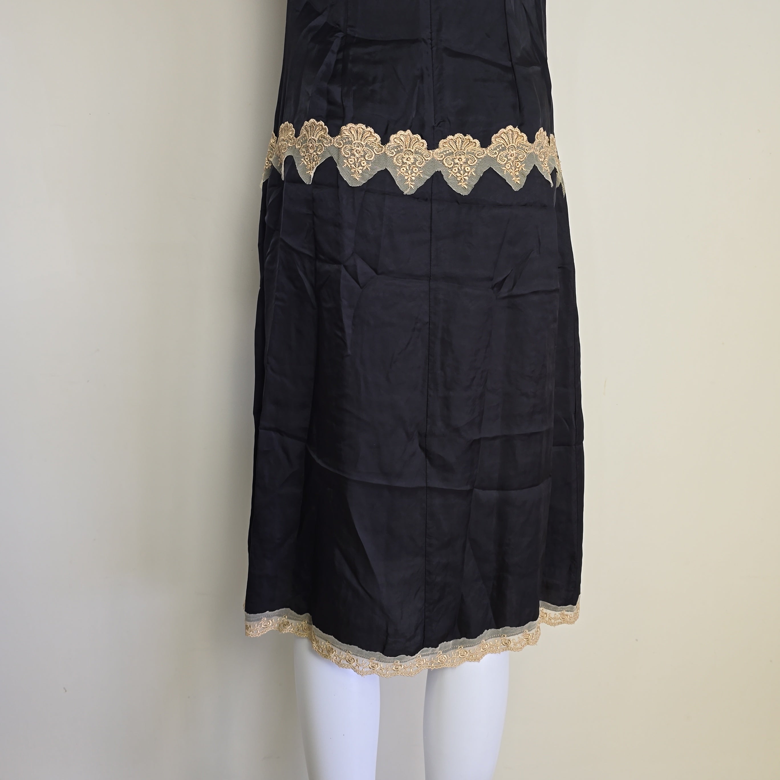 Black skirt with gold lace trim on a white mannequin against a beige background