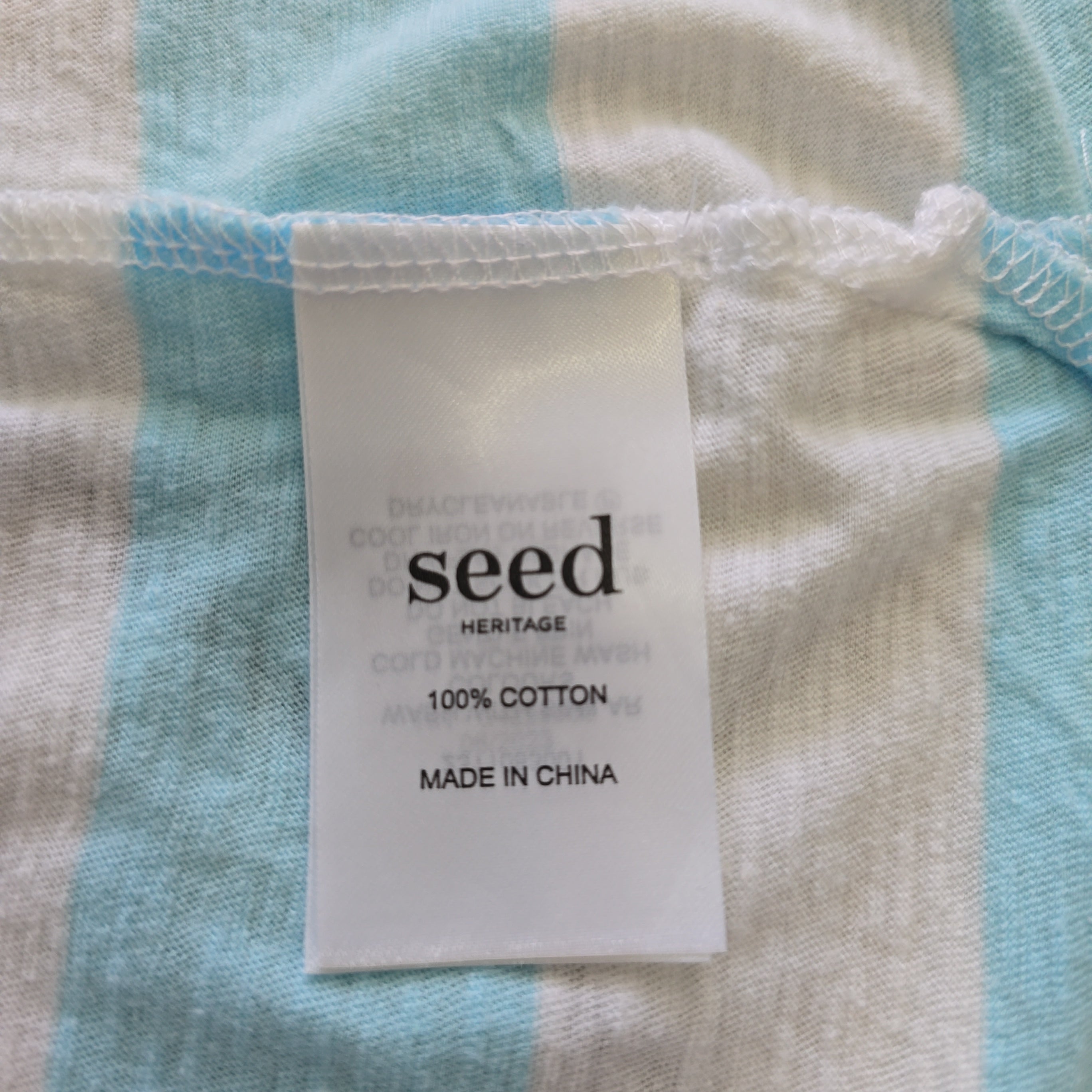 Close-up of a fabric with a 'seed' label on a blue and beige striped background