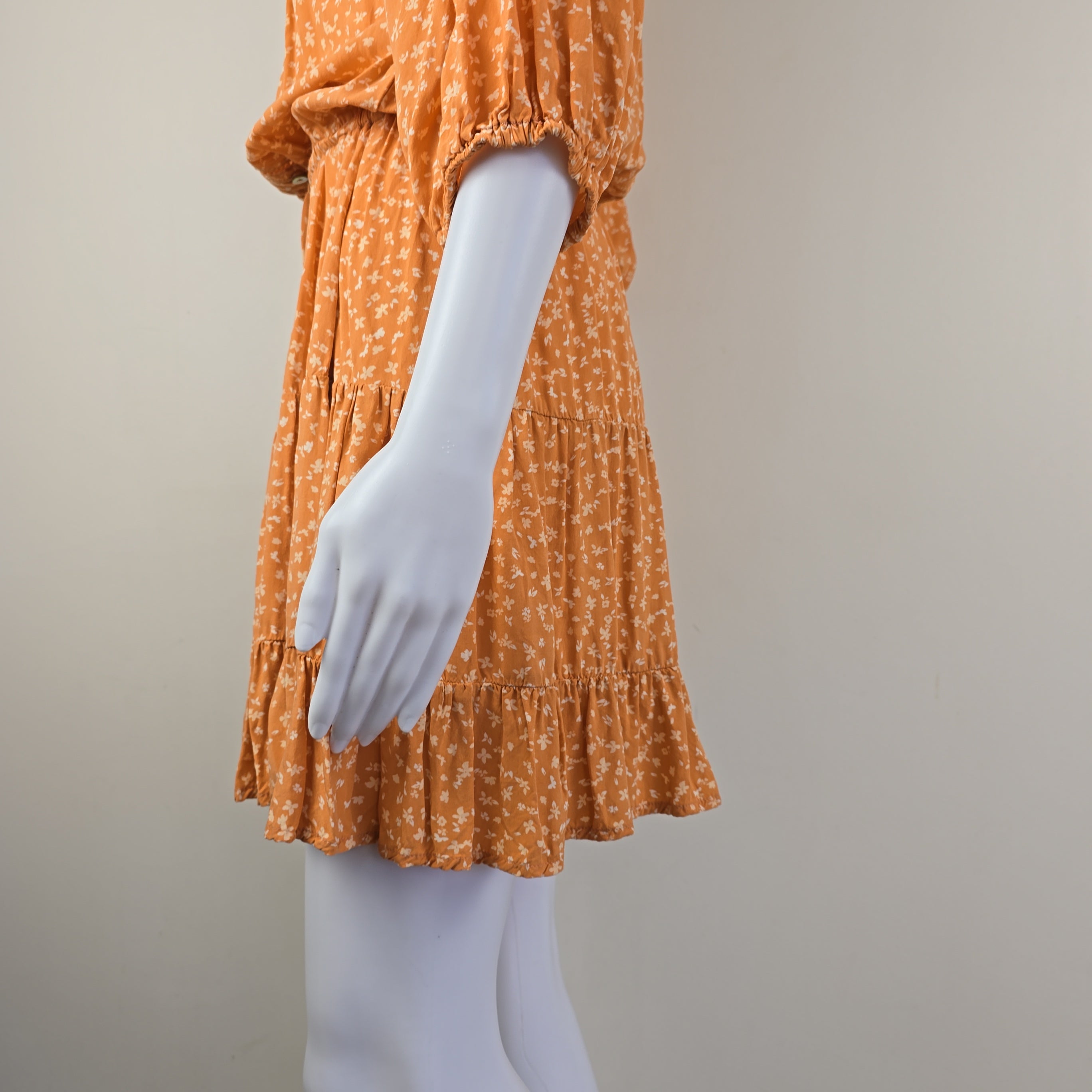 Mannequin arm wearing an orange patterned garment with a white plastic hand.