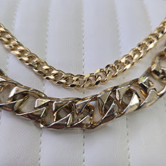 Two gold chains on a white textured surface