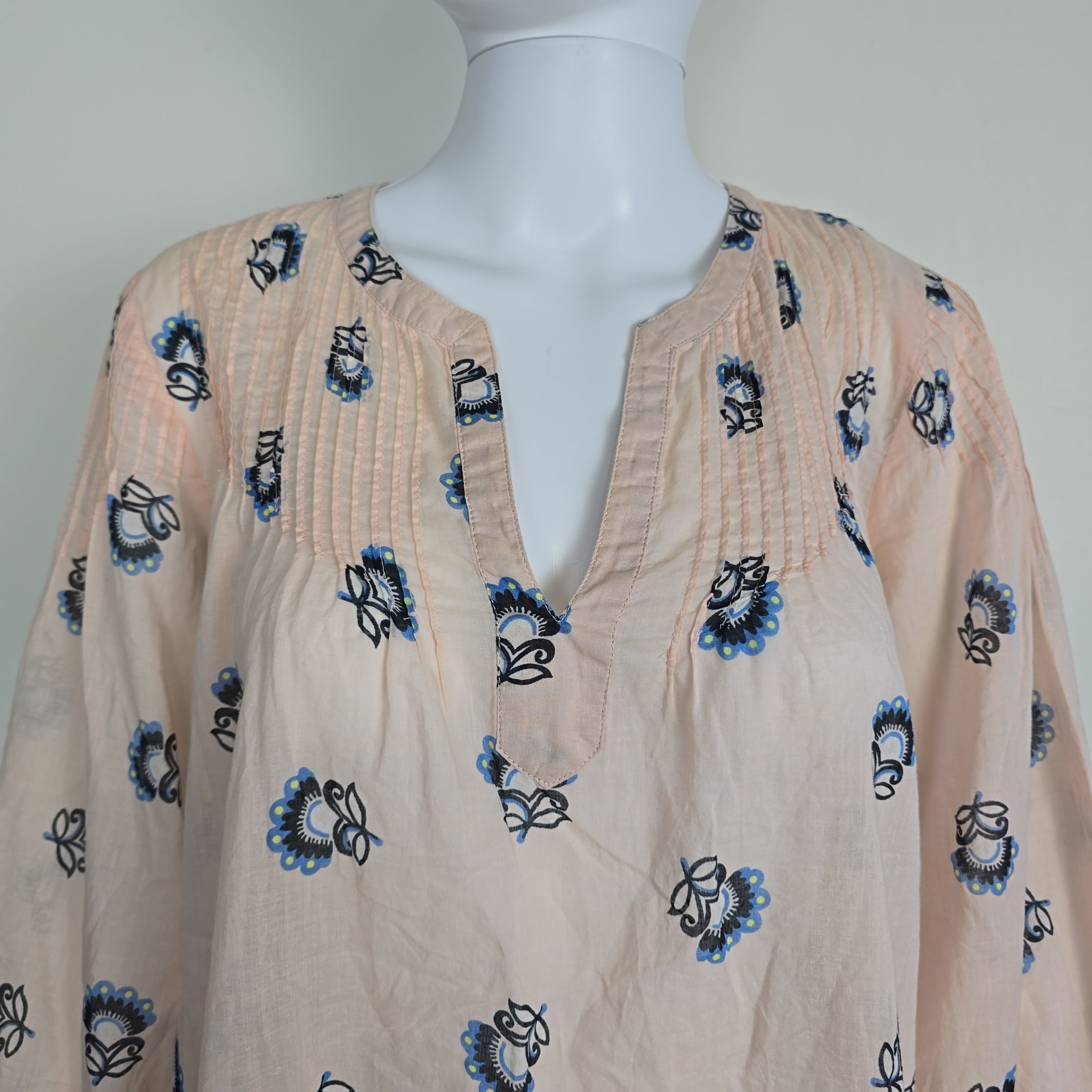 Mannequin wearing a beige top with black and blue floral patterns on a plain background