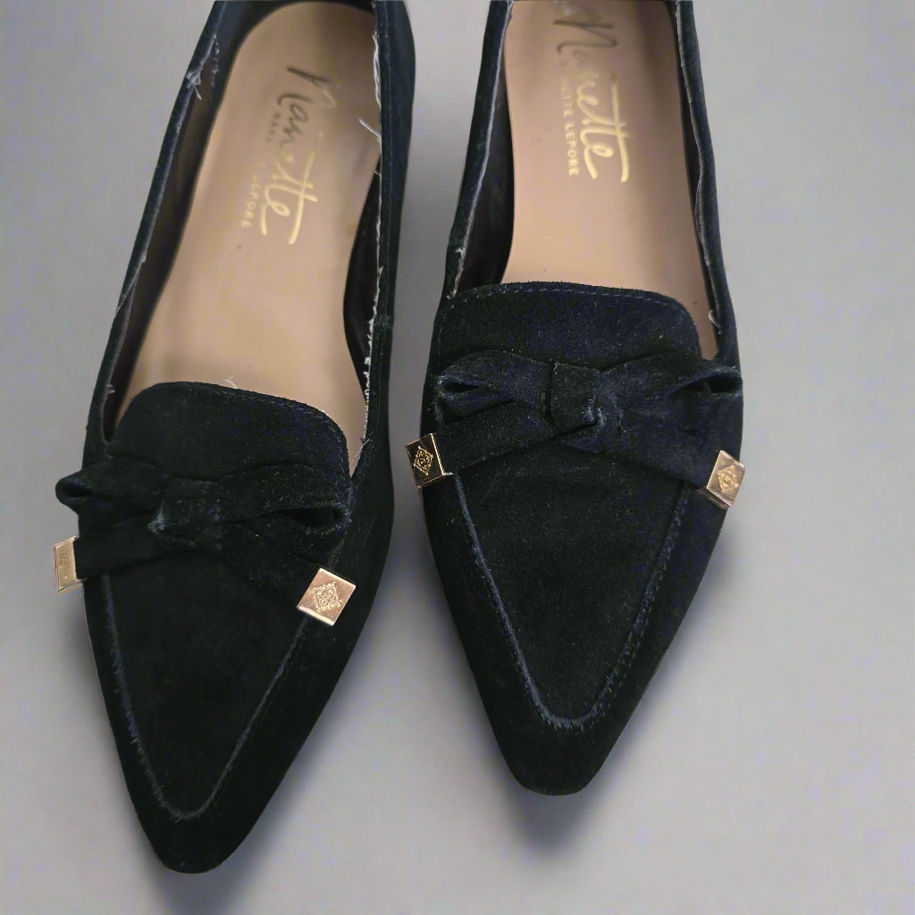 Pair of black suede shoes with a bow detail on a light background