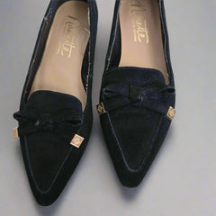 Pair of black suede shoes with a bow detail on a light background