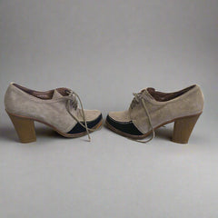 Pair of brown suede shoes hanging on a white wall.