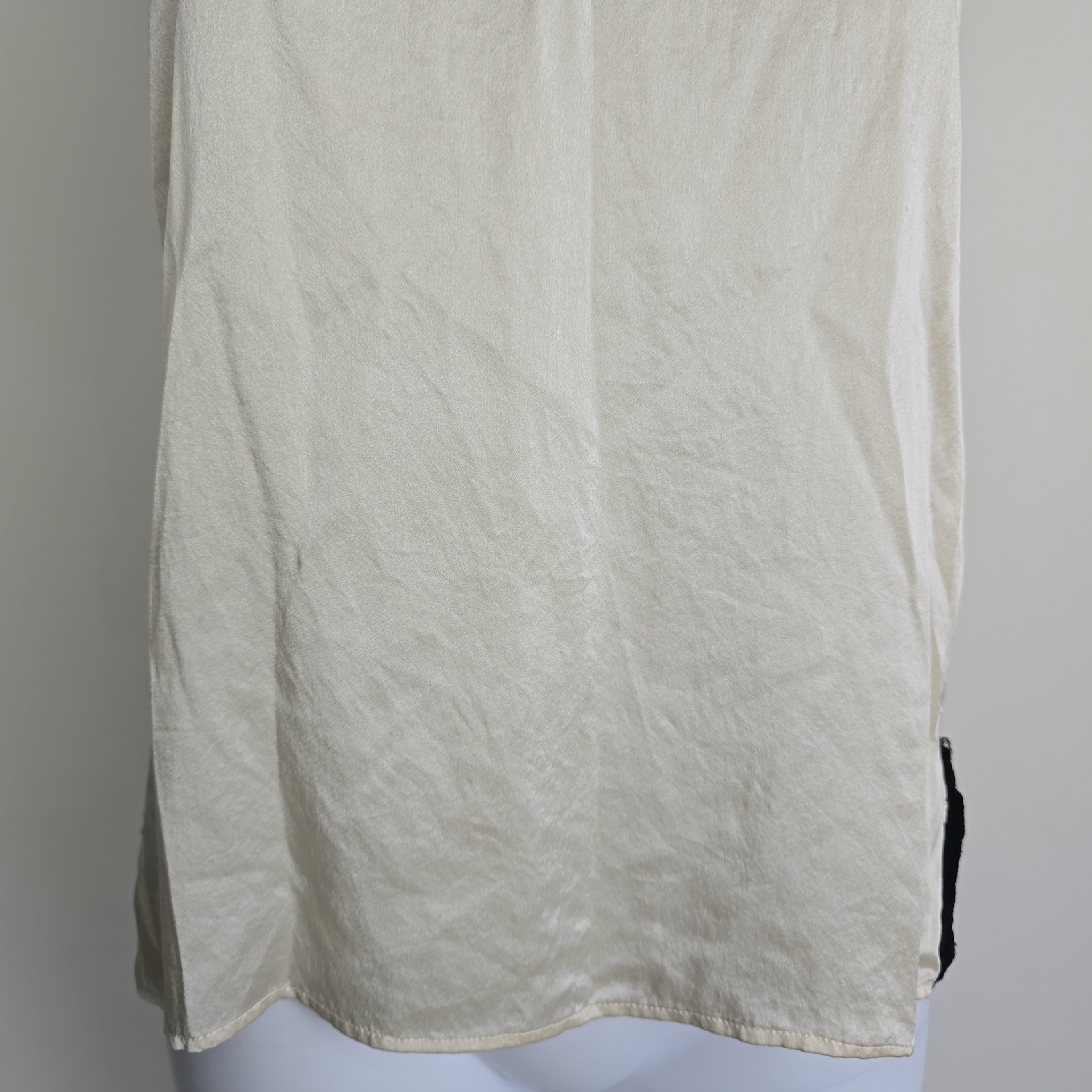 Mannequin wearing a white top with black lace details on a plain background