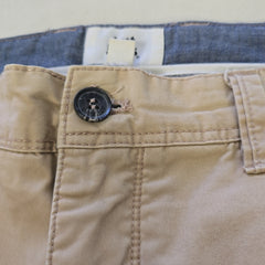 Close-up of beige pants with a button, with blue jeans partially visible in the background.
