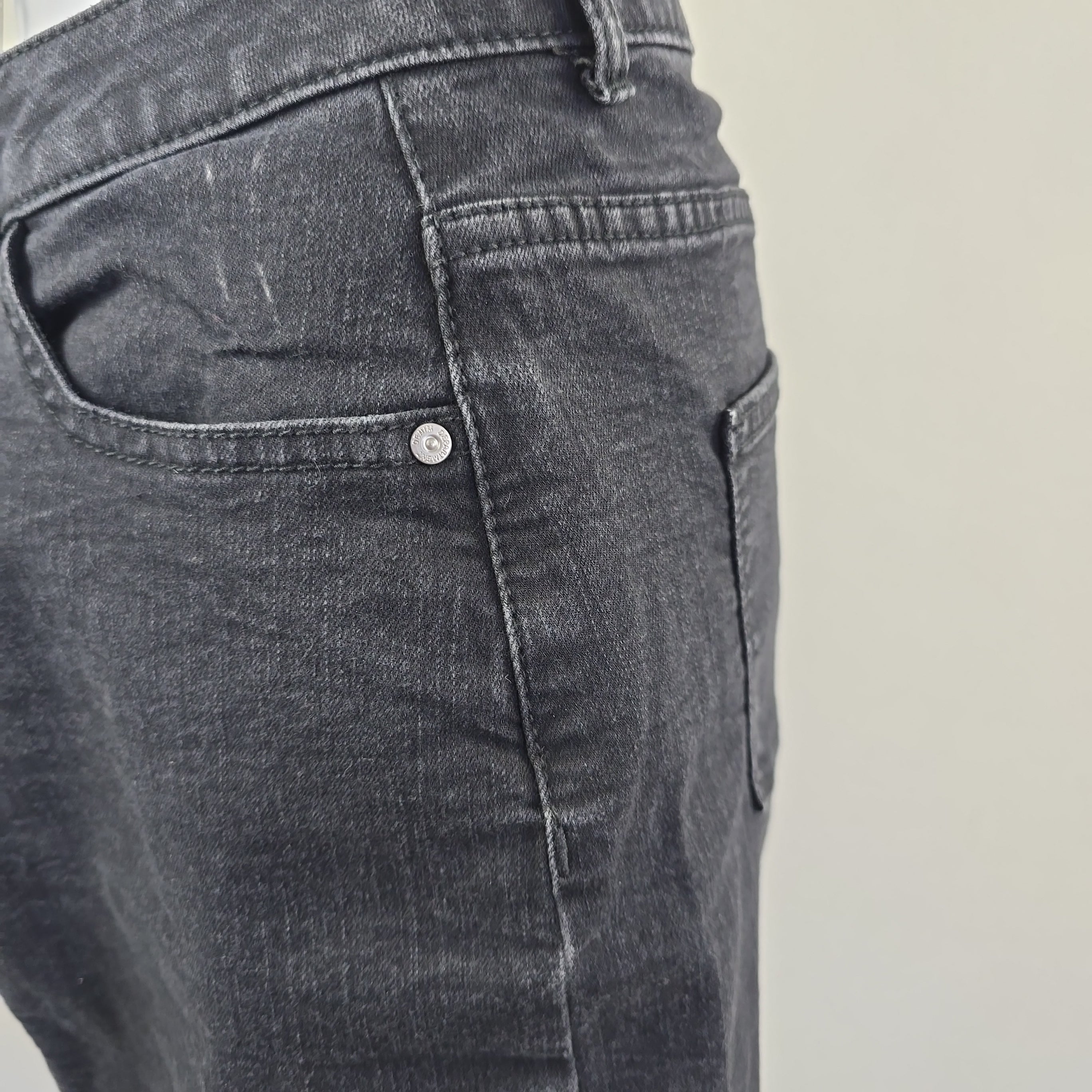 Close-up of a gray denim pocket with a button on a plain background