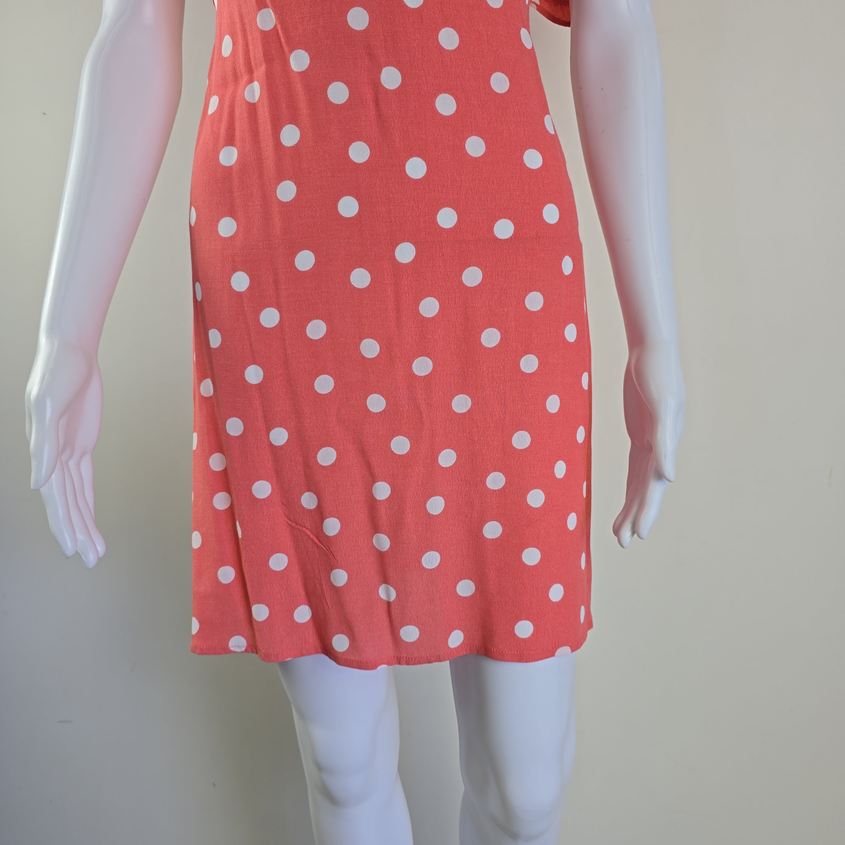 Red dress with white polka dots on a mannequin against a plain background