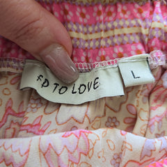 Fabric with a label reading 'FP TO LOVE' held by a hand against a colorful fabric background.
