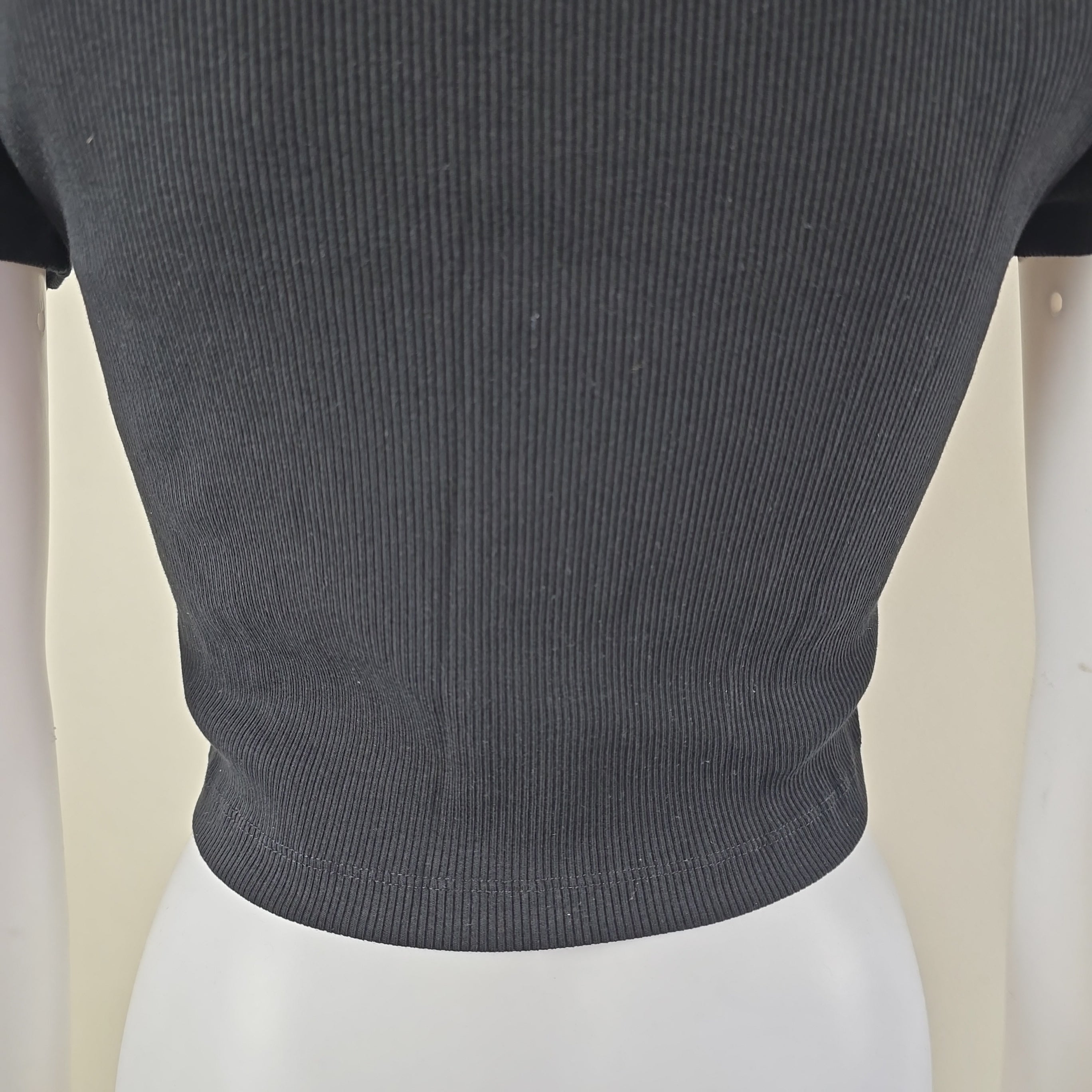 Close-up of a dark gray ribbed top sleeve on a mannequin against a beige background