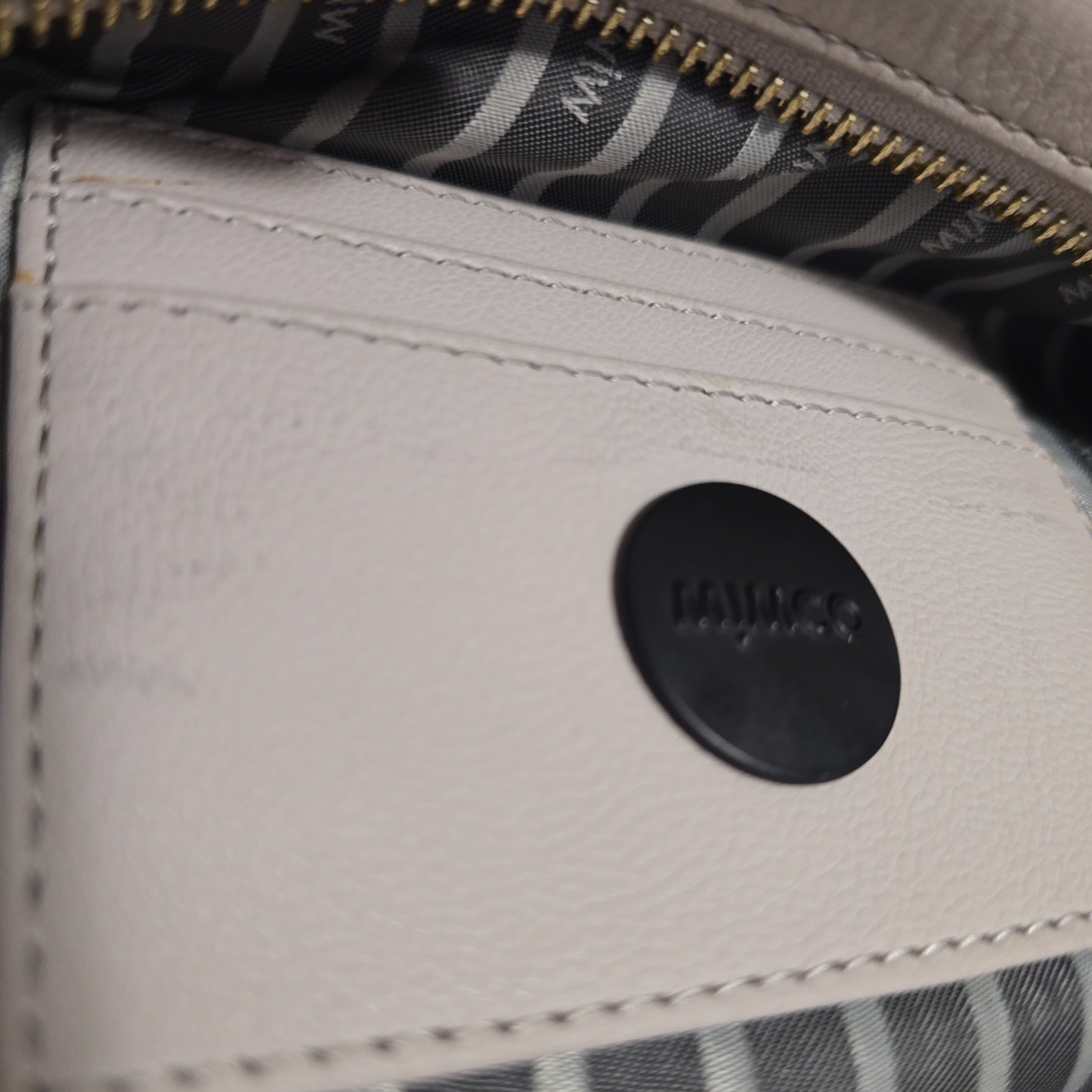 Close-up of a grey leather bag with a black label featuring Mimco text.