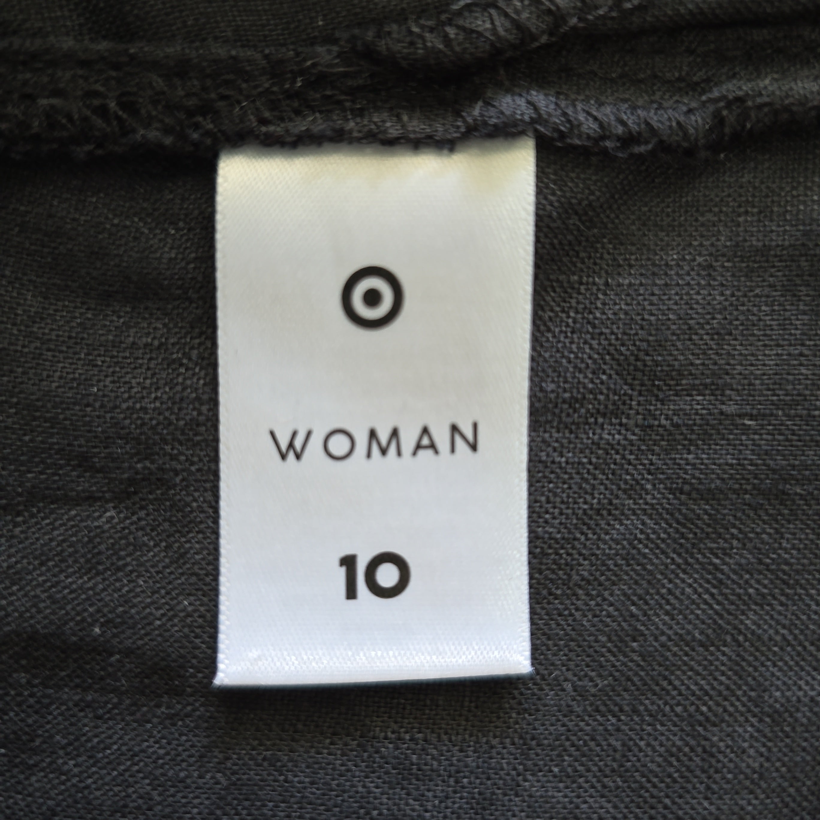 Clothing tag with 'Woman 10' on a dark fabric background