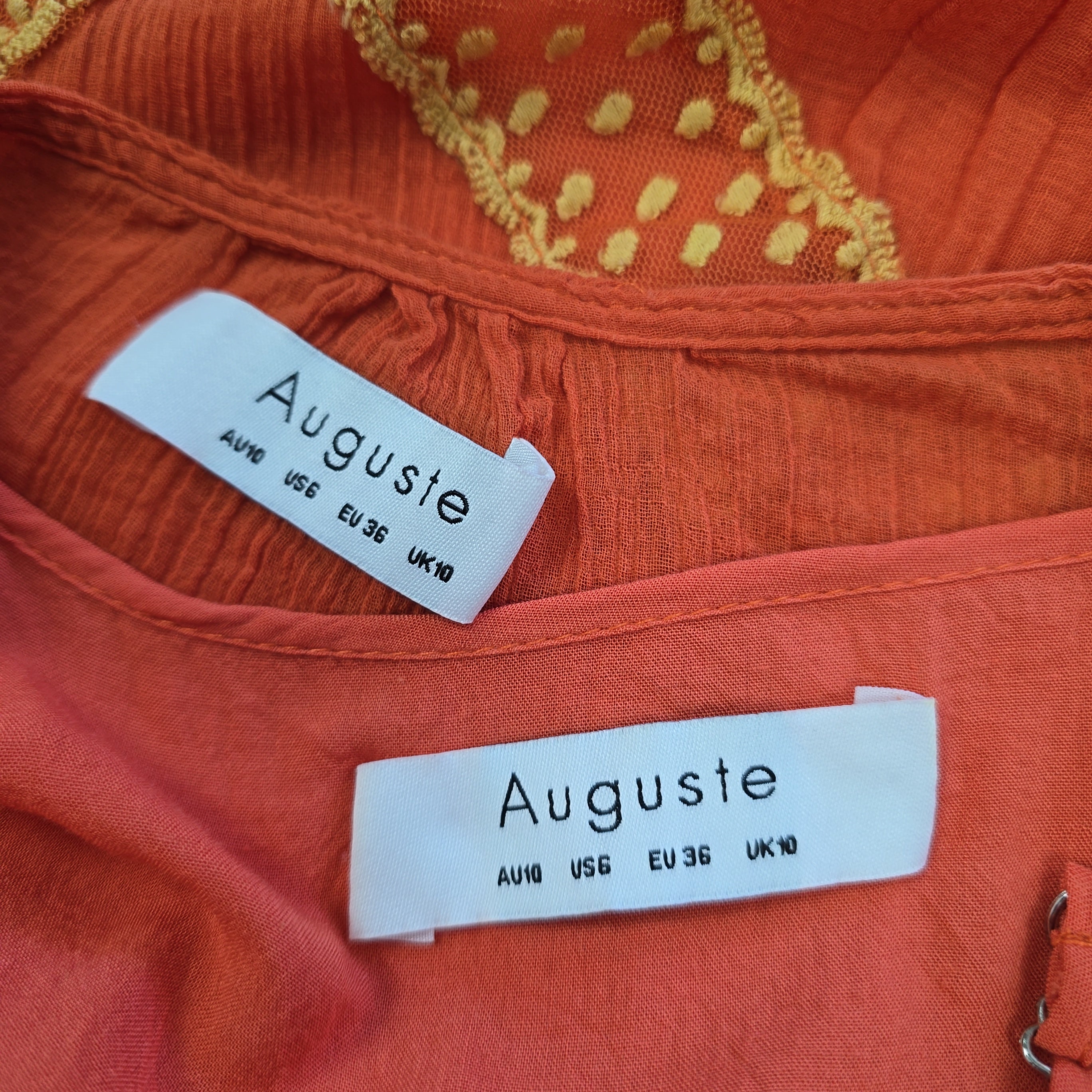 Close-up of an orange garment with 'Auguste' labels on a textured fabric background.