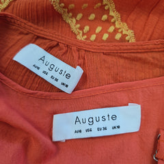 Close-up of an orange garment with 'Auguste' labels on a textured fabric background.