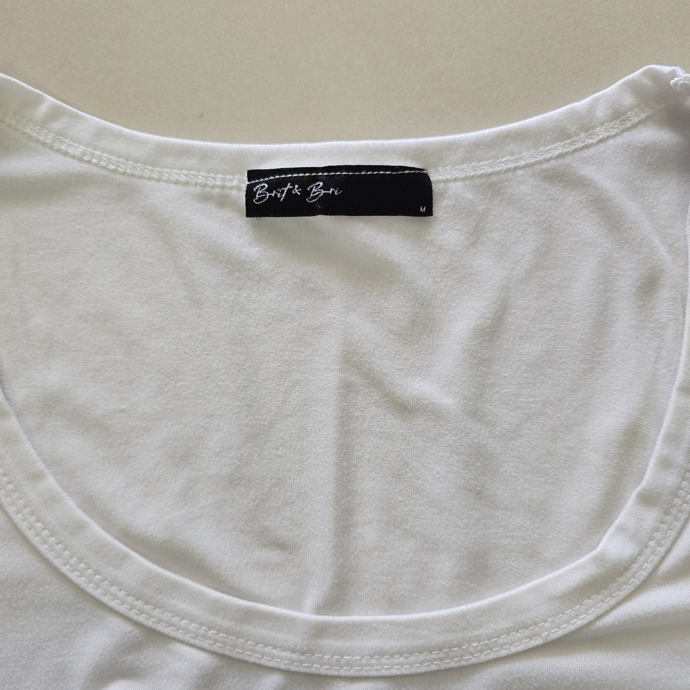 Close-up of a white tank top with a black label on a beige background