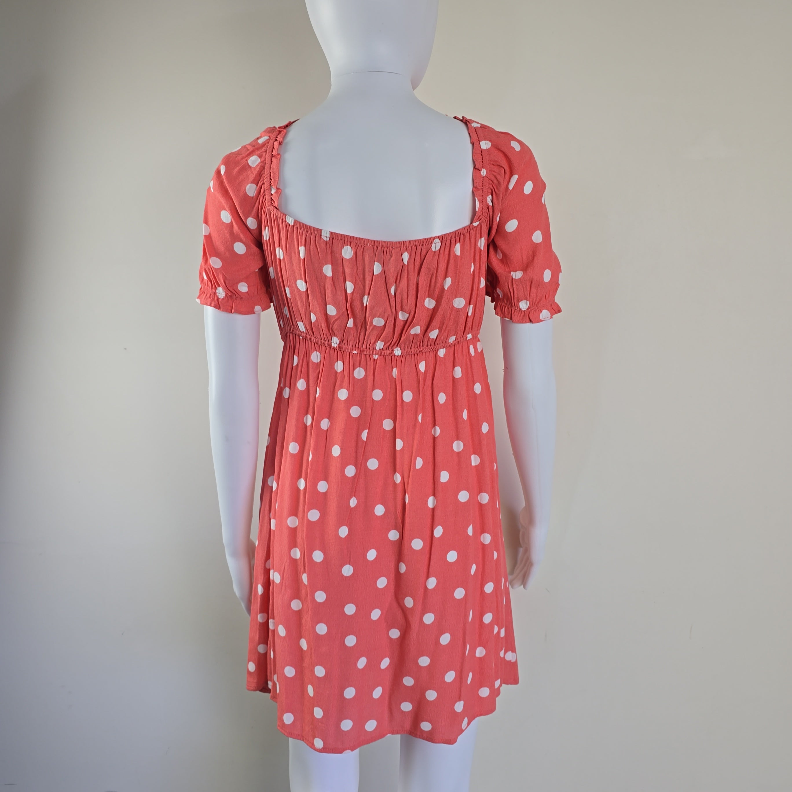 Red dress with white polka dots on a mannequin against a plain background