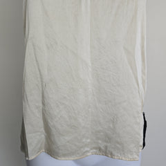 Mannequin wearing a white top with black lace details on a plain background